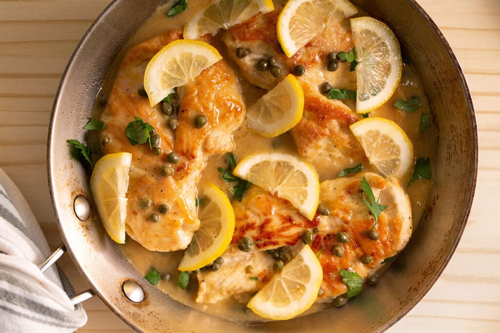 top view of chicken piccata in a pan on top of a wooden table