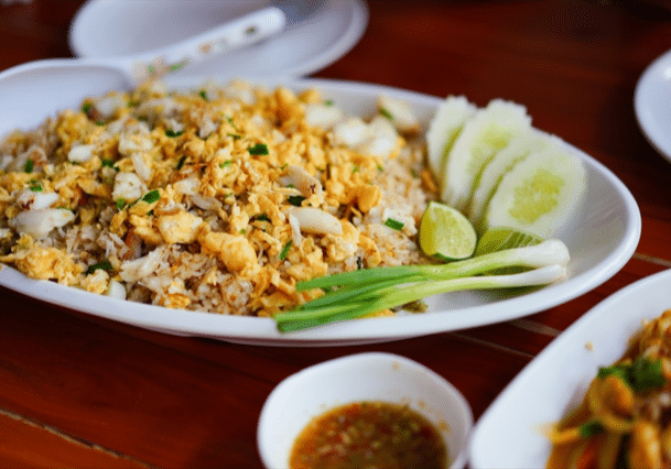 a plate of crab fried rice with green onions, sliced lime and sliced cucumber
