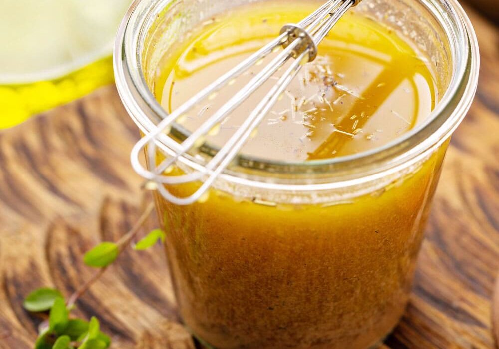 a jar of lemon garlic marinade with a silver whisk on top of the jar placed on a brown wooden chopping board