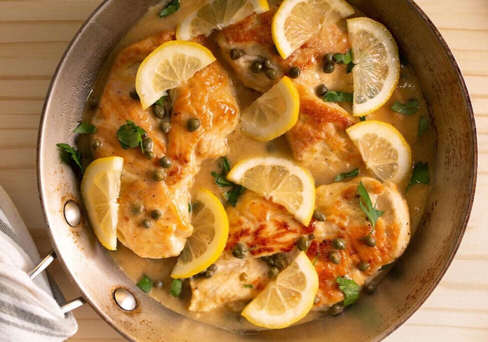 top view of chicken piccata in a pan on top of a wooden table